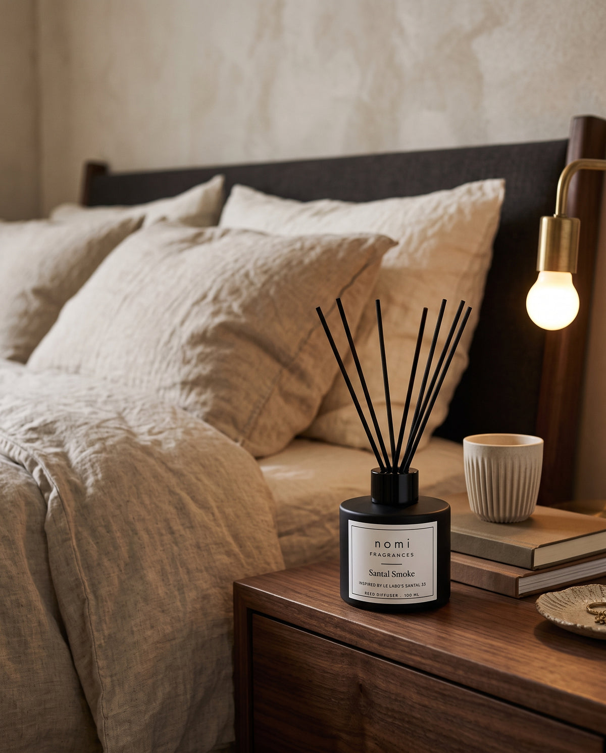 Santal Smoke reed diffuser in the round black bottle on a bedroom nightstand